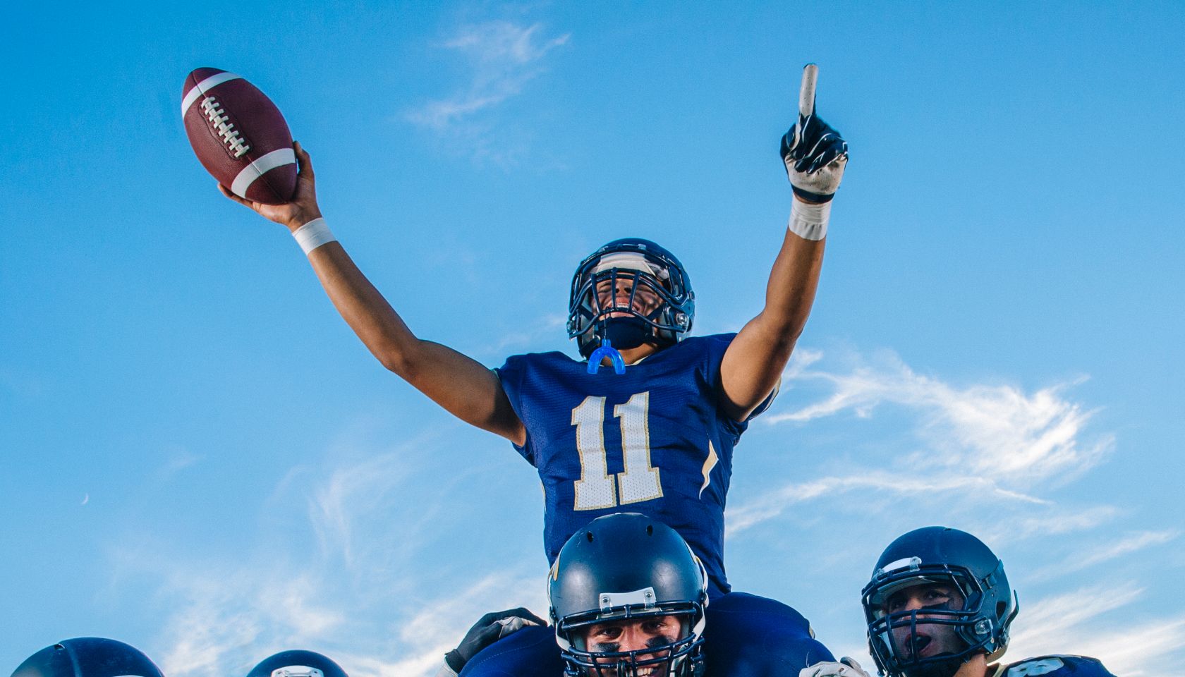 Five teenage and young adult american football players celebrating with shoulder carry