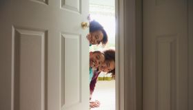 Portrait of Black sisters peeking from behind door
