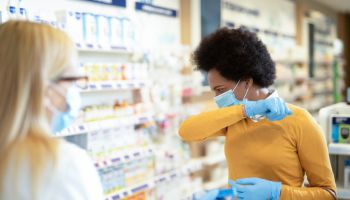 Mid adult woman with protection mask and gloves coughing and buying a medicine.