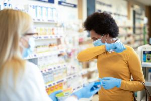 Mid adult woman with protection mask and gloves coughing and buying a medicine.
