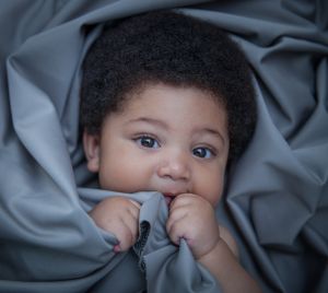 Beautiful black baby in bed facing camera smiling while holding on to the bedsheet