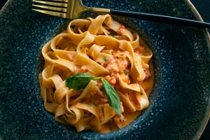 Vegetarian or vegan Italian pasta in tomato sauce. Cooking and serving vegan food at home, in a cafe or restaurant. Spaghetti with chopped vegetables, in a beautiful plate, on the dining table.