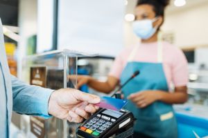 Employee in supermarket serving senior customer with face mask