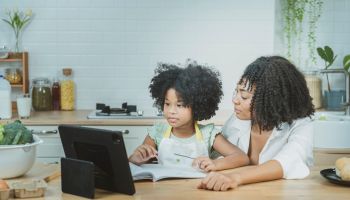 A single mother and African American daughter are teaching their children homework and studying online with their children by greeting friends and teachers or video calling with their father on his way home. By the way, the house prepares to cook food. in