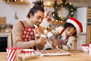 Happy ethnic family father and son in aprons making Christmas cookies together at home