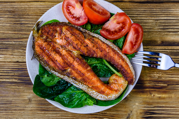 Plate with roasted salmon steak, tomtoes and spinach leaves on a wooden table