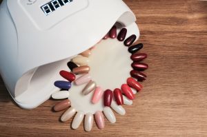 Top view of UV led gel nail drying lamp and nail polish color swatch on the manicure table.