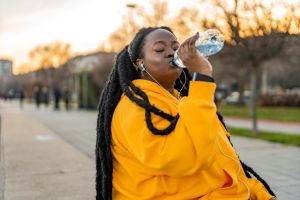 Young curvy woman in sportswear drinking water while sitting after exercising