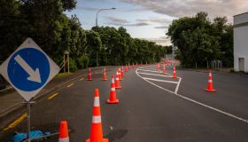 Orange traffic cones lined up on the road. Board with blue arrow pointing to the right to divert traffic. Auckland.