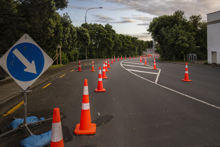 Orange traffic cones lined up on the road. Board with blue arrow pointing to the right to divert traffic. Auckland.