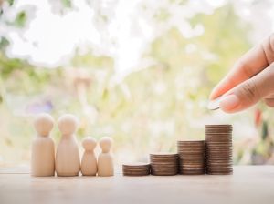 Close up hand putting coins to stack of coins with wooden human figure for saving concept