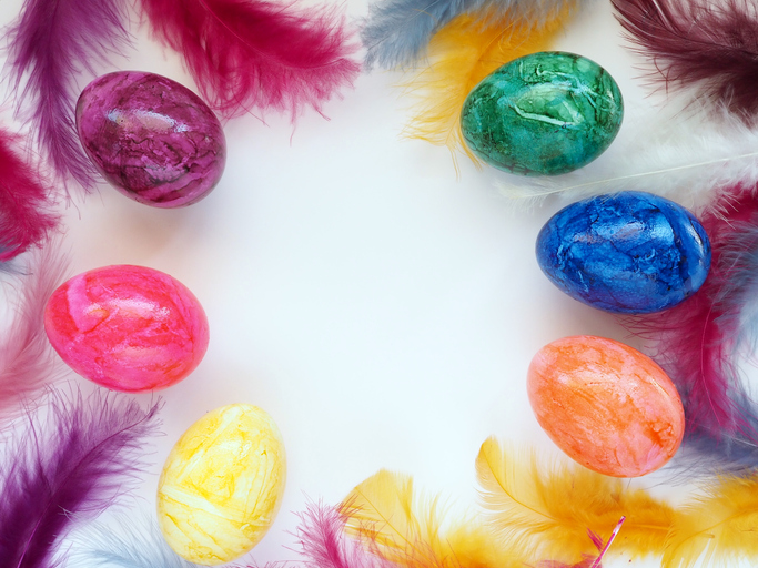 Multi-colored Easter eggs and bird feathers are laid out on a white table