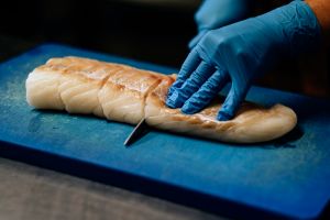 close-up on hands in blue latex gloves cutting raw fish on chopping board