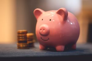 A ceramic piggy bank on a blue sofa with stacks of coins.