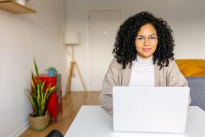 Latin American young woman with laptop computer smiling at camera sitting on table in the living room at home