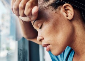 Doctor, black woman stress or anxiety by window in hospital, workplace and tired in healthcare job, pain or headache. Burnout nurse, sad or exhausted in medical clinic or depression in health clinic