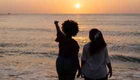 girls walking while holding her hands on sandy beach and enjoying picturesque sunset