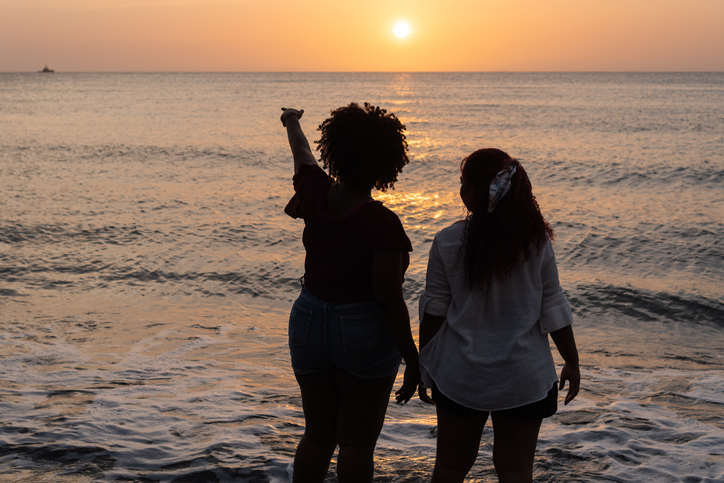 girls walking while holding her hands on sandy beach and enjoying picturesque sunset