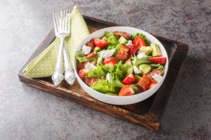 Homemade fresh salad of strawberries, avocado, bacon, lettuce, feta cheese close-up in a bowl. Horizontal