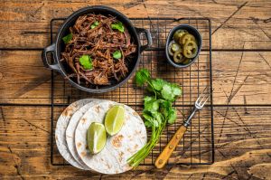 Cooking of mexican pork carnitas taco. Wooden background. Top view