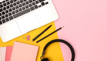 Layout with laptop, headphones and stationery on a yellow and pink background.