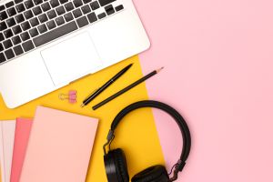 Layout with laptop, headphones and stationery on a yellow and pink background.