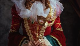 Closeup on medieval queen in red dress with venetian mask