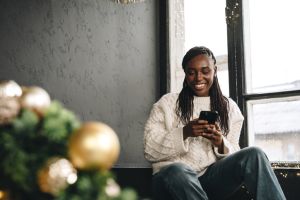 Young beautiful African woman using her phone at home decorated for Christmas season