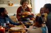 Happy black mature woman serving Thanksgiving turkey to her family at dining table.