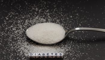 White crystal sugar on a small spoon with the inscription diabetes. Campaign to reduce sugar consumption.