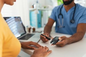 Diabetologist doctor testing blood sample on blood sugar meter in diabetes clinic. Doctor holding glucometer with test strip, waiting for results. Paediatric diabetes in teenage girl, young woman.