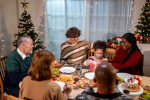 Multi-ethnic family giving gift box to daughter during Christmas party. Attractive little girl receive present from relative while having dinner celebrate holiday Thanksgiving on dining table in house