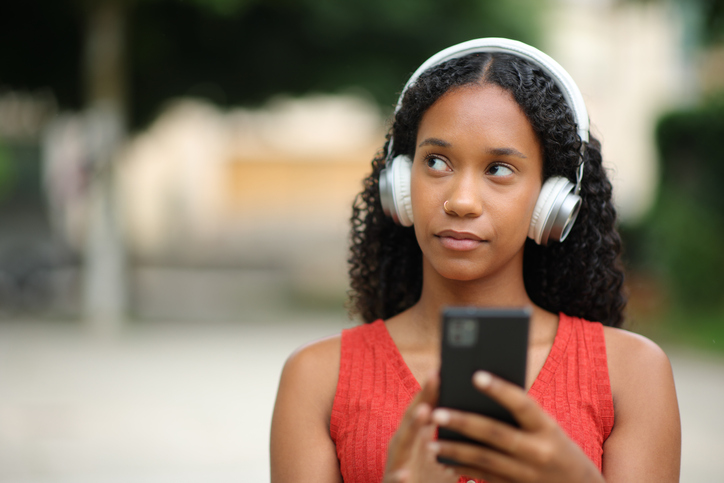 Pensive black woman listening audio in the street