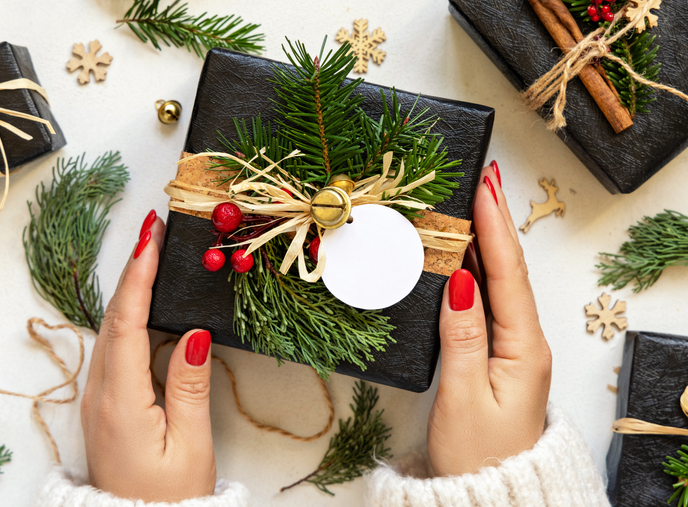 Hands with Christmas present with round blank gift tag, with fir branches and decor, Mockup