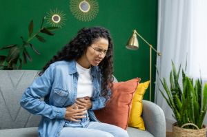 A woman sits on a couch while clutching her stomach in discomfort