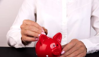 Woman Putting Coin In Piggy Bank, Indoors