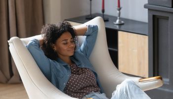 Peaceful smiling young Black woman resting in cozy soft armchair