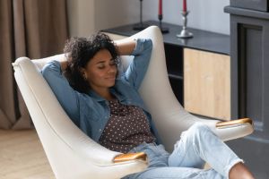 Peaceful smiling young Black woman resting in cozy soft armchair