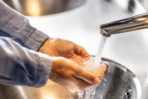 A view of a woman washing her hands under running water in a bathroom.