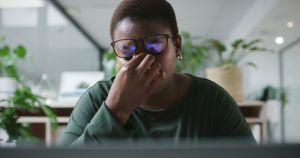 Woman, headache and tired with office desk, fatigue or work life balance with overworked employee. Discomfort, mental health in workplace with African female person, stressed or burnout in job