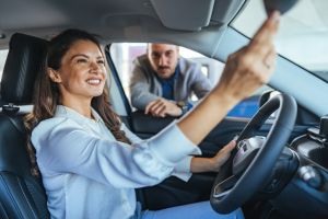 Happy Woman Examining Car with Salesman at Dealership