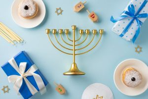 A Hanukkah scene featuring a menorah surrounded by gifts, dreidels, and traditional sweets on a blue background