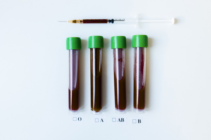 Blood test vials and syringe on a white background, labeled with blood groups O, A, AB, and B