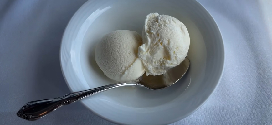 Delicious Vanilla Ice Cream Scoops in a White Bowl with Silver Spoon, on a soft fabric surface