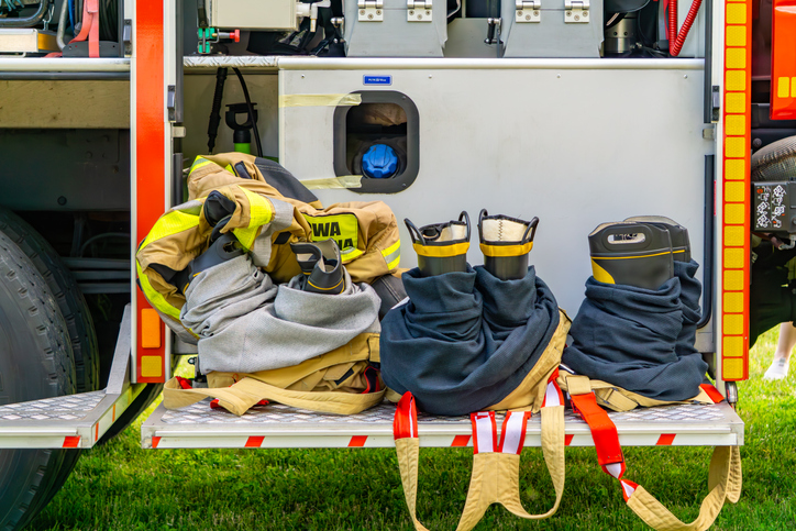 Firefighting gear ready for action – boots, pants, and jackets arranged on the side platform of a fire truck.