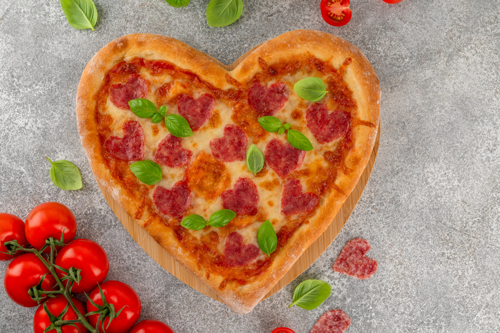 Heart shaped Italian pizza with salami, cheese and fresh basil on a concrete background. Holiday concept for Valentine's day. Top view. Copy space