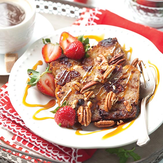A plate with a slice of French toast topped with strawberries, pecans, and a drizzle of syrup, accompanied by a cup of coffee.