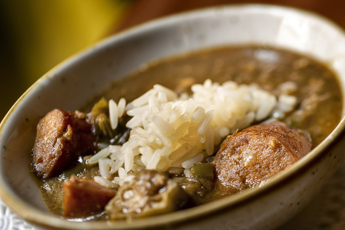 A bowl of savory stew with chunks of meat, vegetables, and white rice.