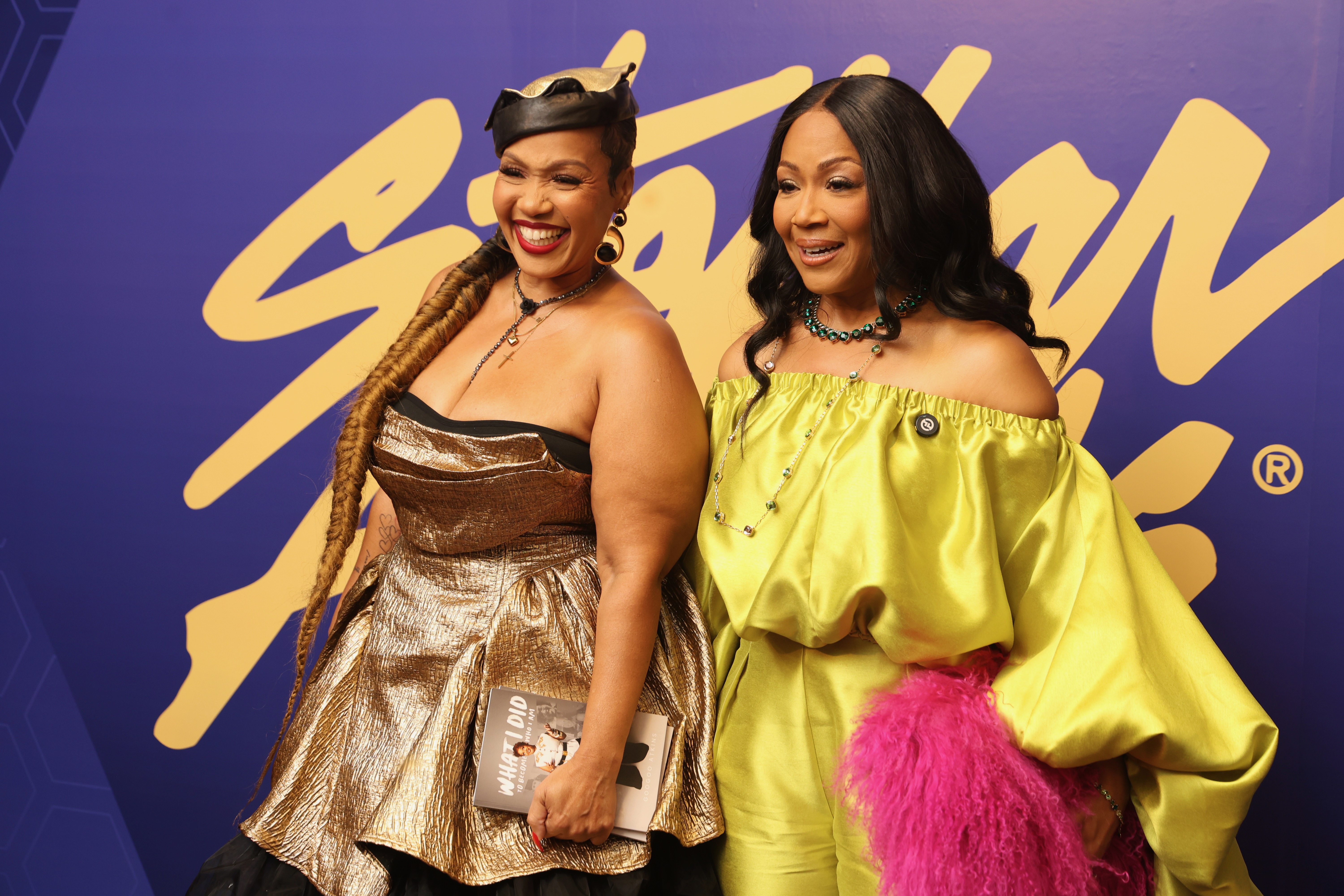 Two women in colorful, stylish outfits posing together in front of a purple and yellow background with the Starz logo.