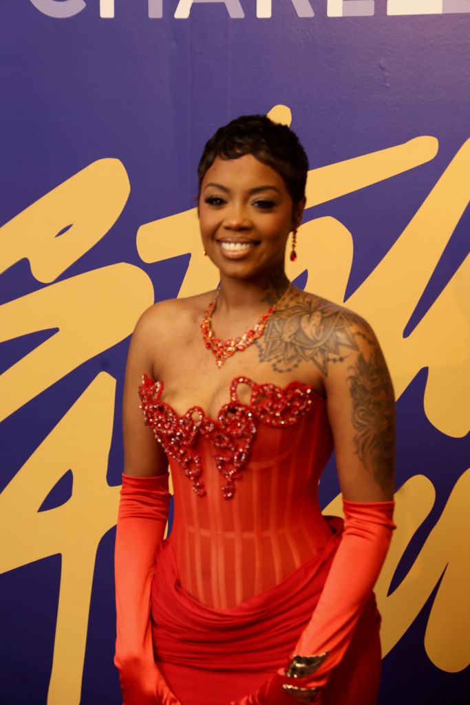 A smiling woman in a red sequined dress and matching gloves stands in front of a purple and yellow background.